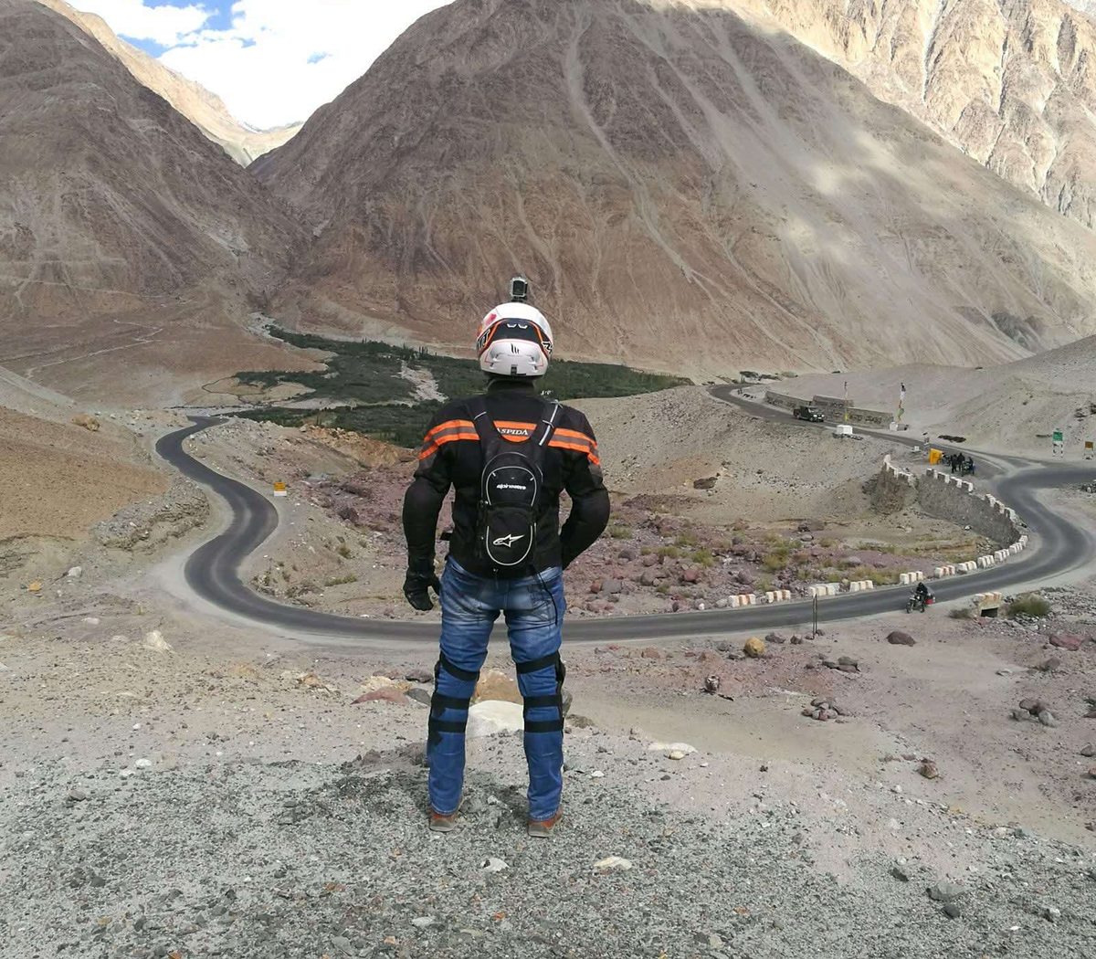 Abhijith B R in riding gear above a winding mountain road in the Himalayas
